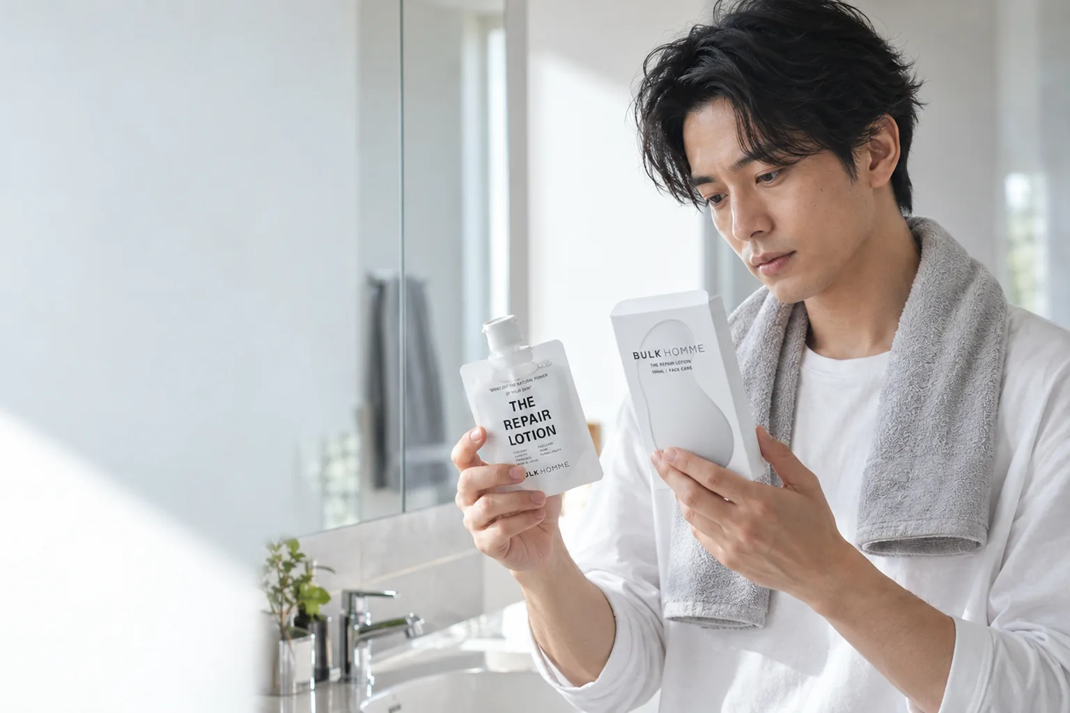 薬用化粧水のパウチと箱を両手に持つ、タオルを肩にかけた白いTシャツの男性の写真
